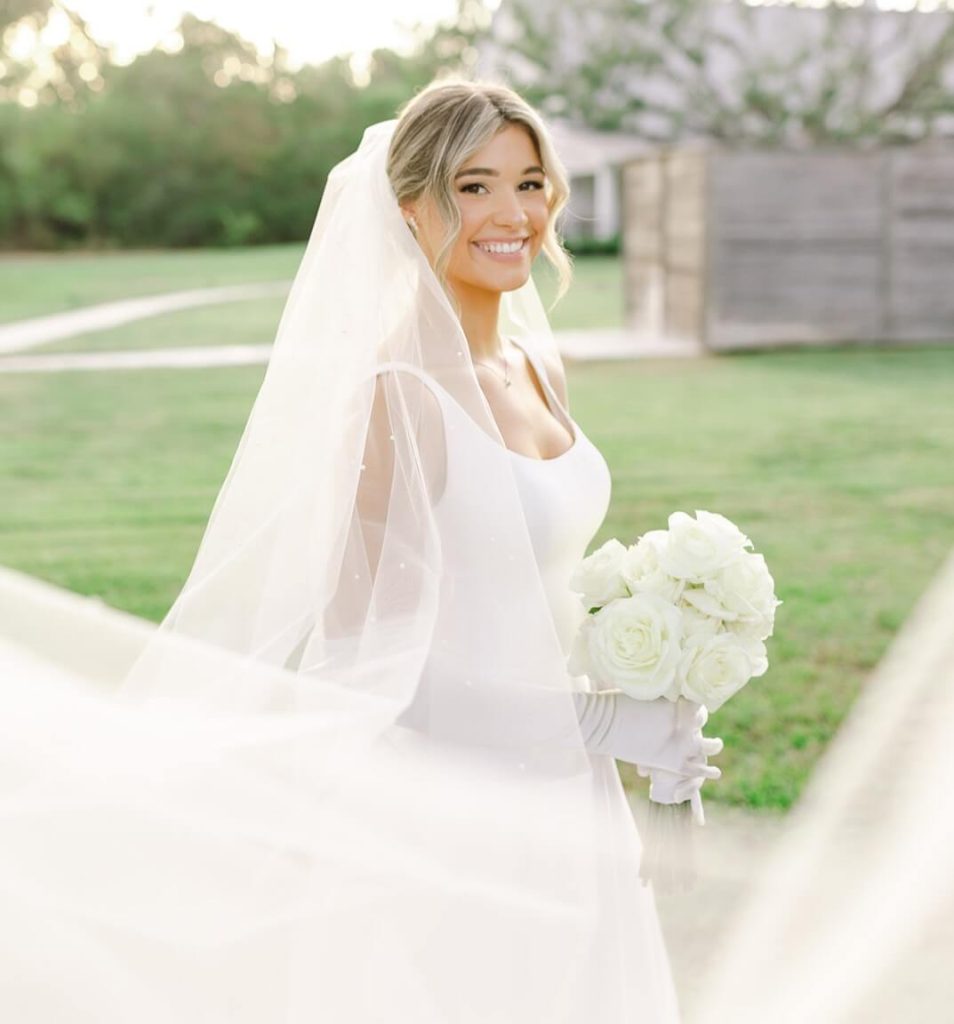 A portrait of a bride in a garden setting, featuring her veil as a decorative element in the composition.