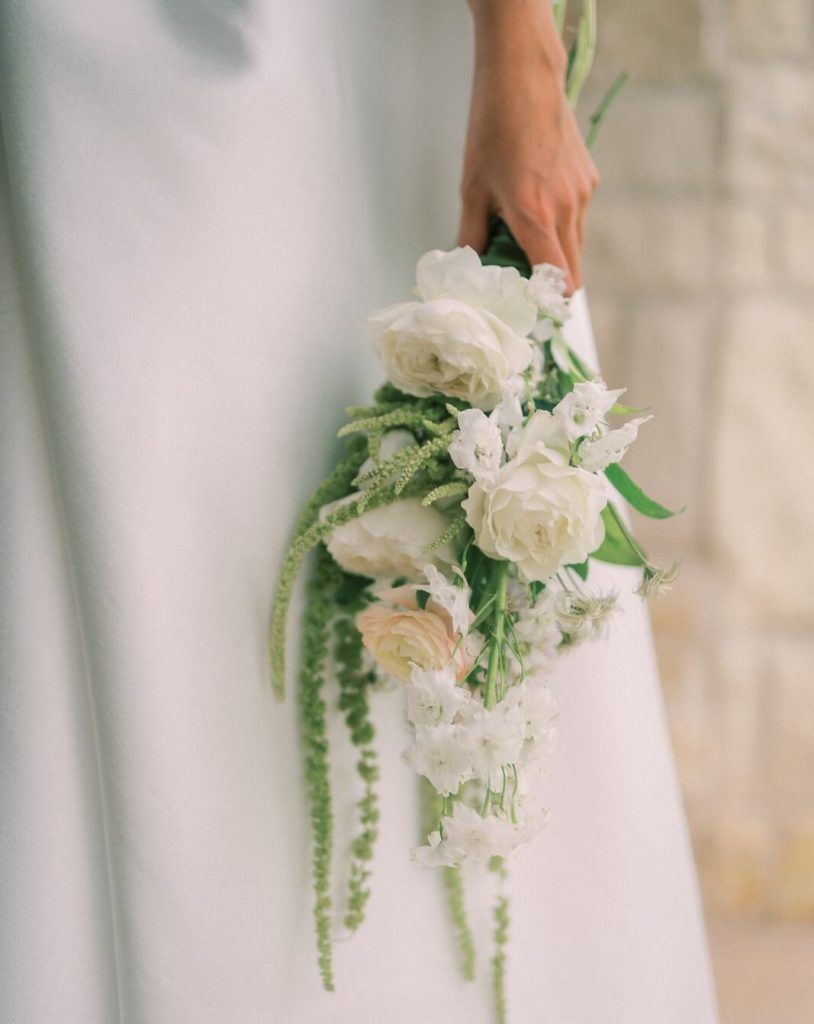 A close-up shot of a bouquet of white roses held by a bride on her wedding dress.