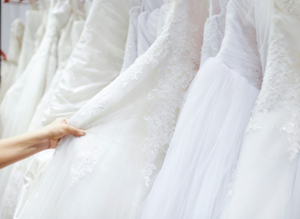 Person browsing through hanging wedding dresses in a bridal shop.