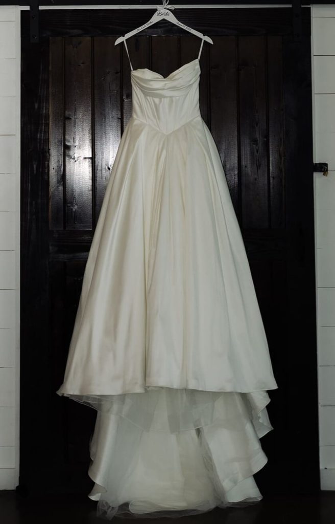 A white satin wedding dress is hung on a wooden door.