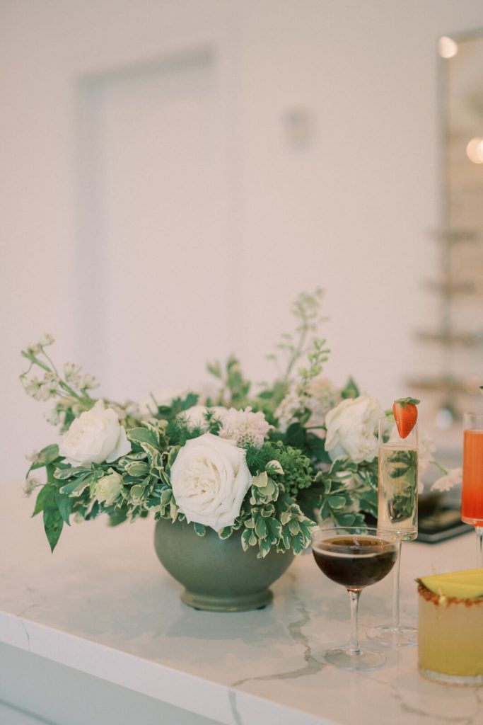 A marble table with a green vase with flowers, and some cocktails.