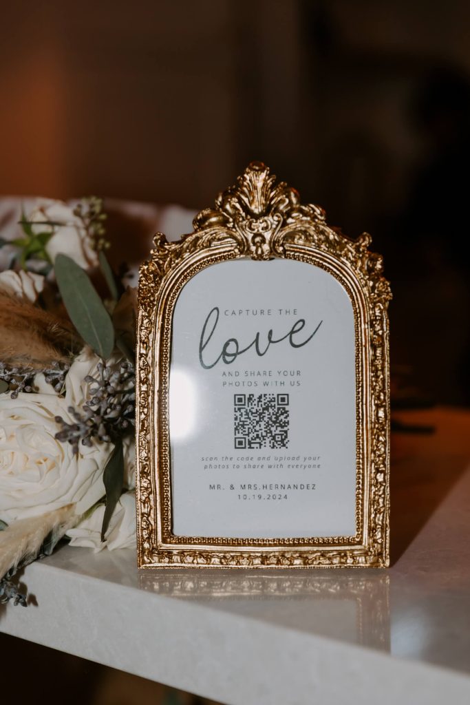 A printed QR code for wedding guests to share their photos with the hosts, set in a golden frame.