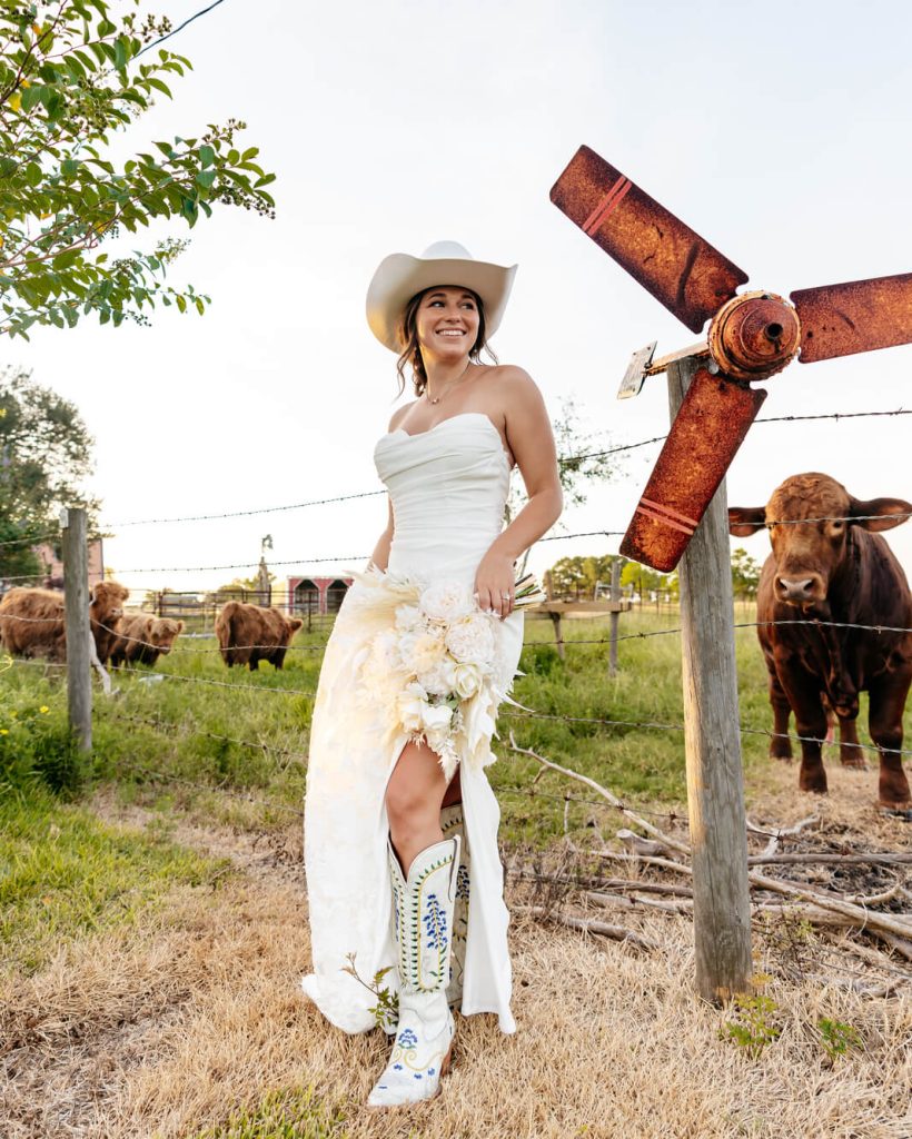 woman in bridal dress wearing a cowboy hat standing next to cattle ranch
