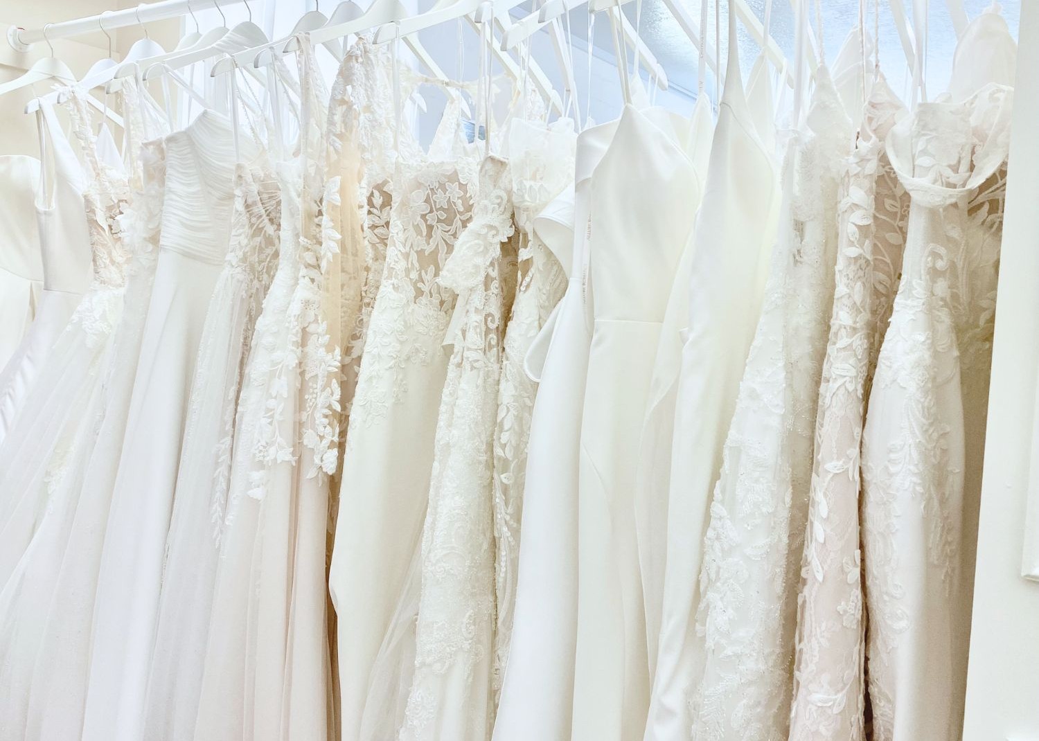 Row of elegant white and ivory wedding gowns hanging on a clothing rack.