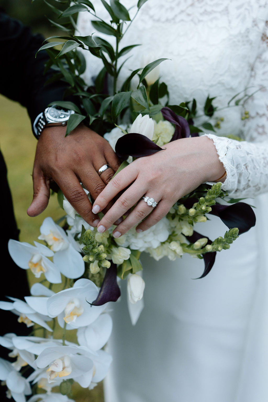 A bride and groom showing off their wedding bands over a bouquet of white flowers.