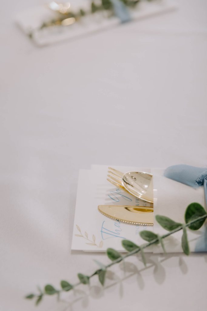 A close-up shot of a wedding's table showcasing the golden cutlery and a stem of eucalyptus.