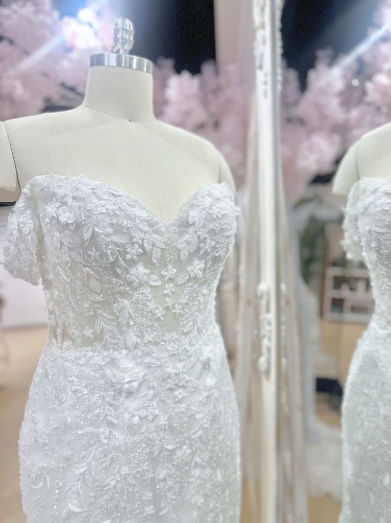 Strapless, form-fitting wedding gown covered in shimmering sequins and lace embellishments on a mannequin.