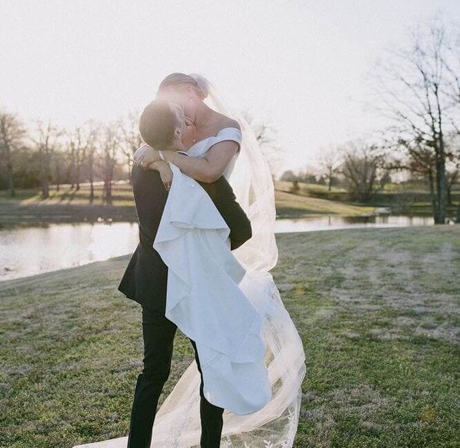 A groom carrying his bride while kissing by the lake.