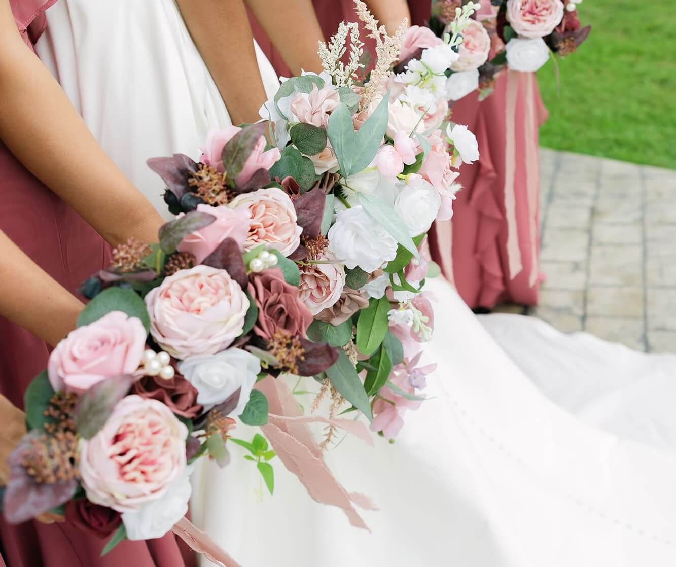 The bride is lined up with her bridesmaids, who are wearing old rose-colored dresses, while holding their bouquets.