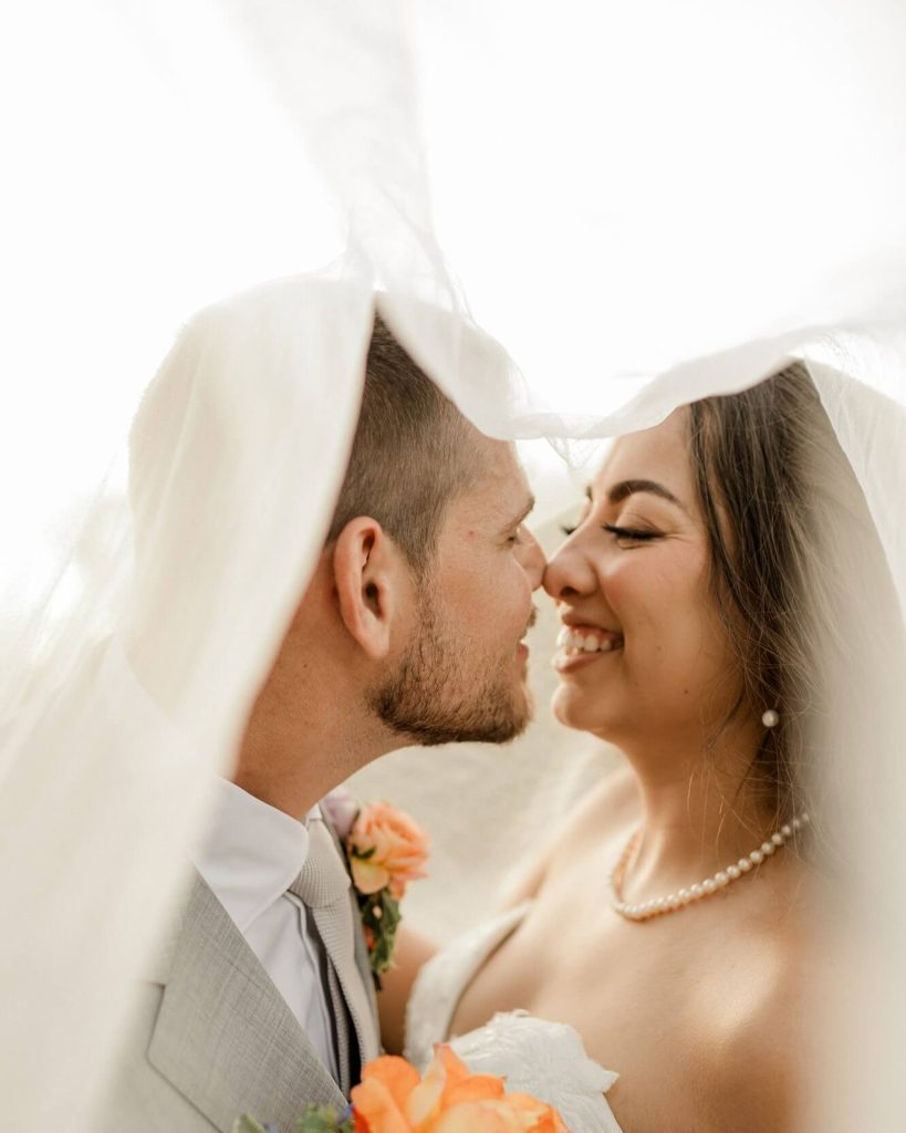 A portrait of a groom and a bride under the veil leaning for a kiss.