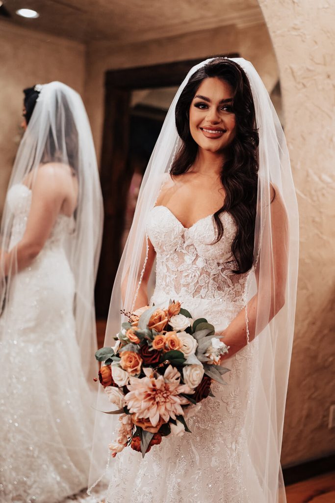 A beautiful bride smiling wonderfully while holding her autumn floral bouquet.