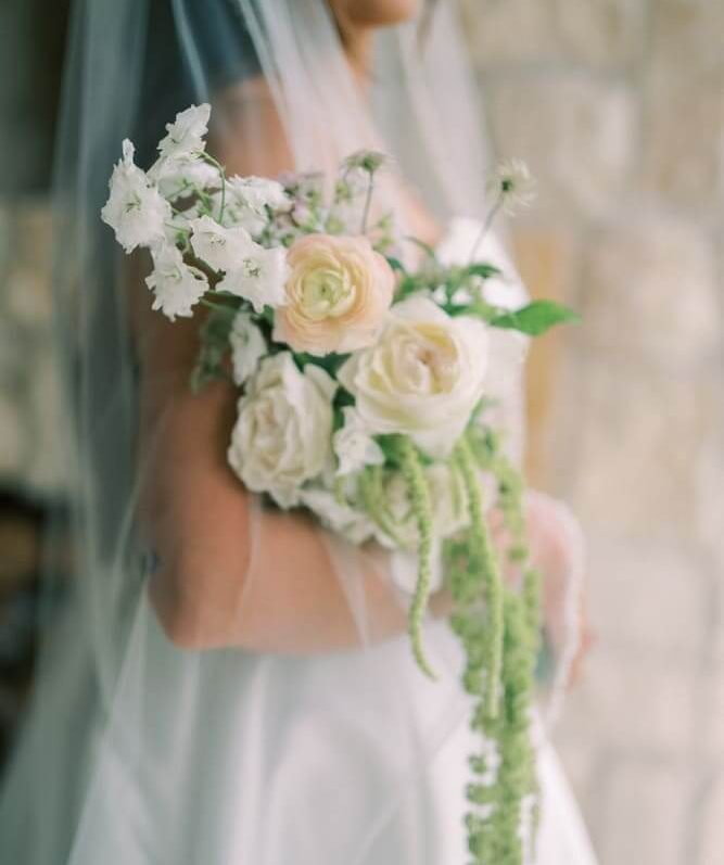 A bride wearing a white wedding dress, and a veil while holding her white bridal bouquet.