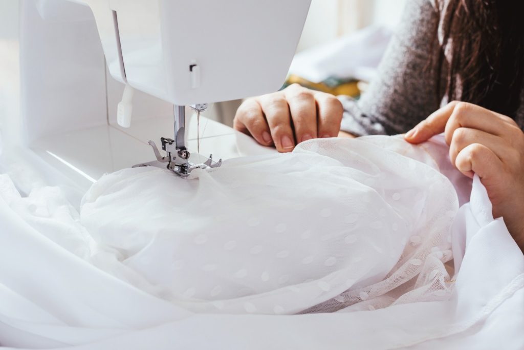 Close-up of hands sewing lace fabric on a wedding dress using a sewing machine.
