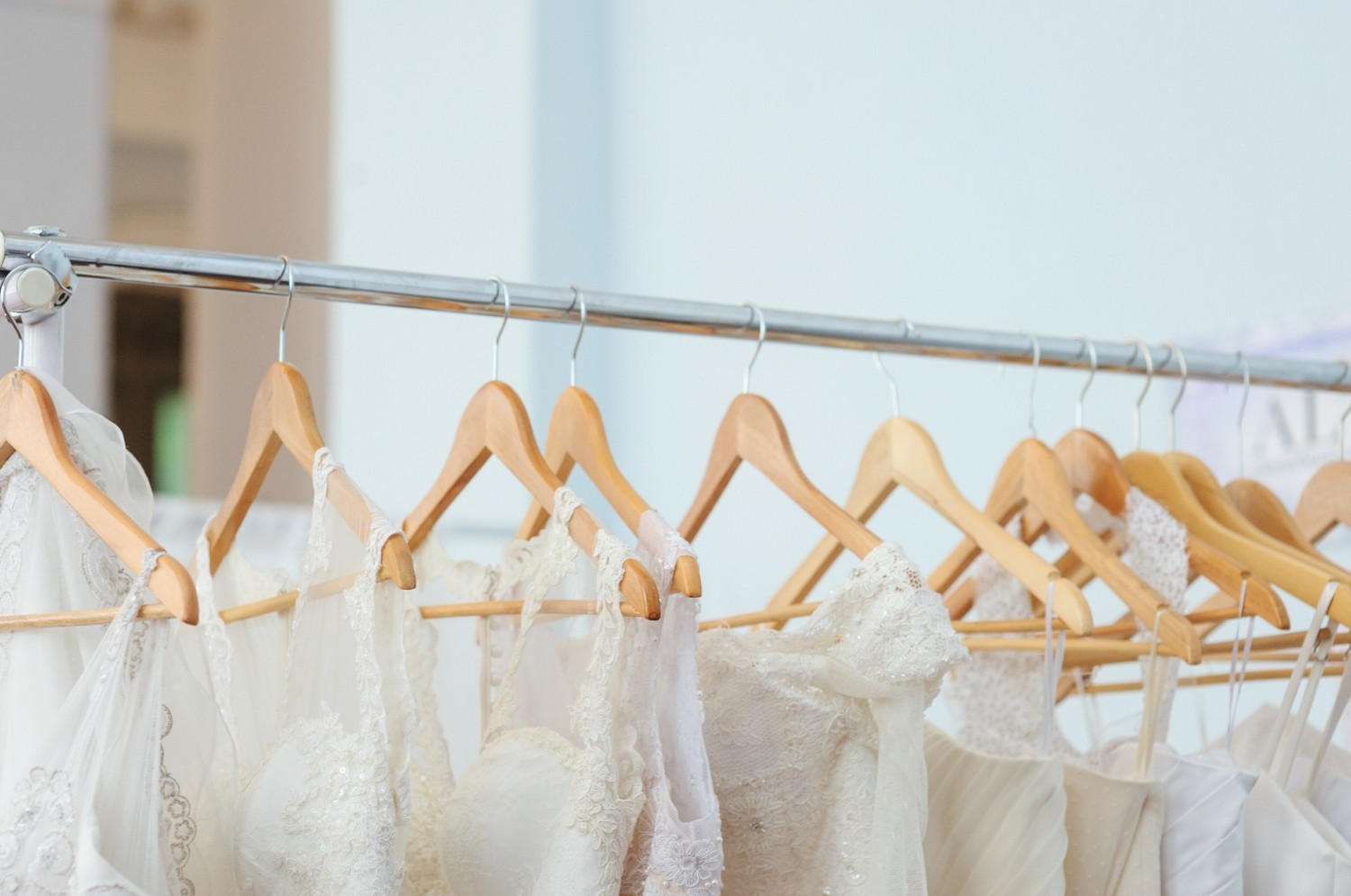 Row of lace and satin wedding dresses neatly arranged on wooden hangers.